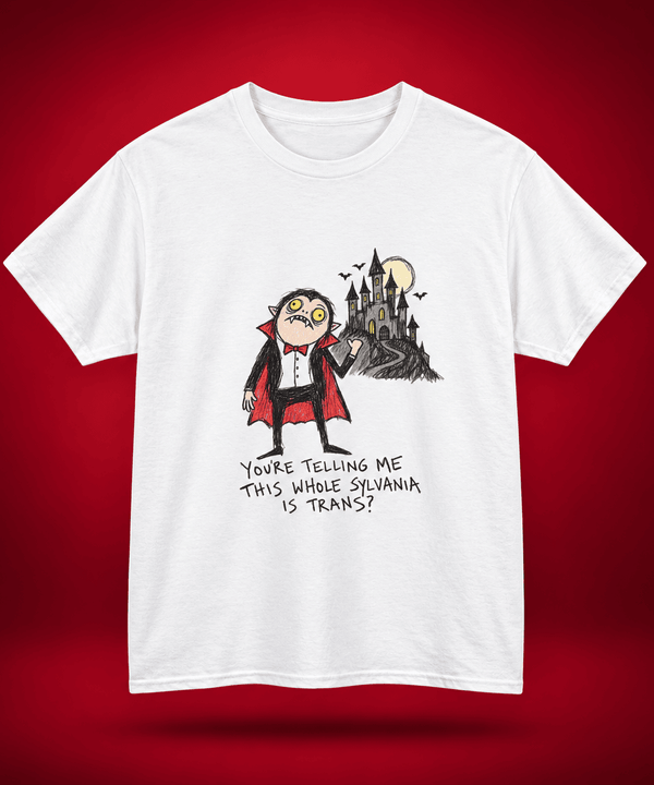 A white short-sleeve crewneck t-shirt featuring a cartoon graphic of a vampire looking surprised next to a haunted castle, with the text 'YOU'RE TELLING ME THIS WHOLE SILVANIA IS TRANS?' printed below. The t-shirt is displayed against a dark red gradient background.