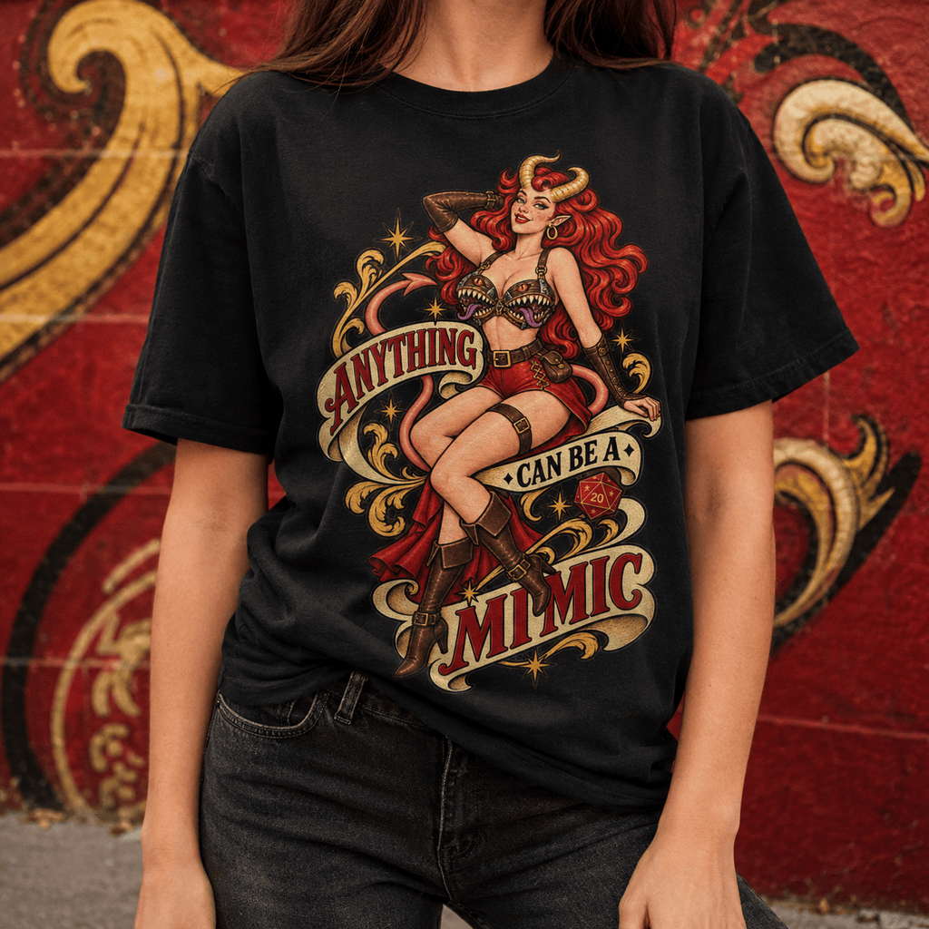 A person wearing a black graphic T-shirt with a large vintage-style pin-up illustration and the text 'ANYTHING CAN BE A MIMIC' in red, cream, and gold tones, standing against a red wall with ornate gold mural details.
