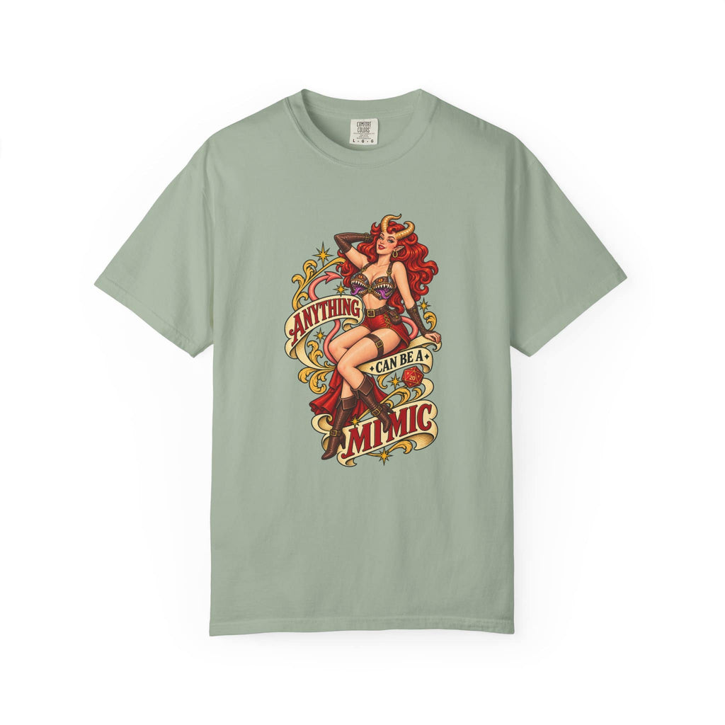 A sage green short-sleeve t-shirt with a vintage-style pin-up graphic on the front. The graphic features a woman with red hair and a red dress, surrounded by retro text that reads 'ANYTHING CAN BE A MIMIC'.