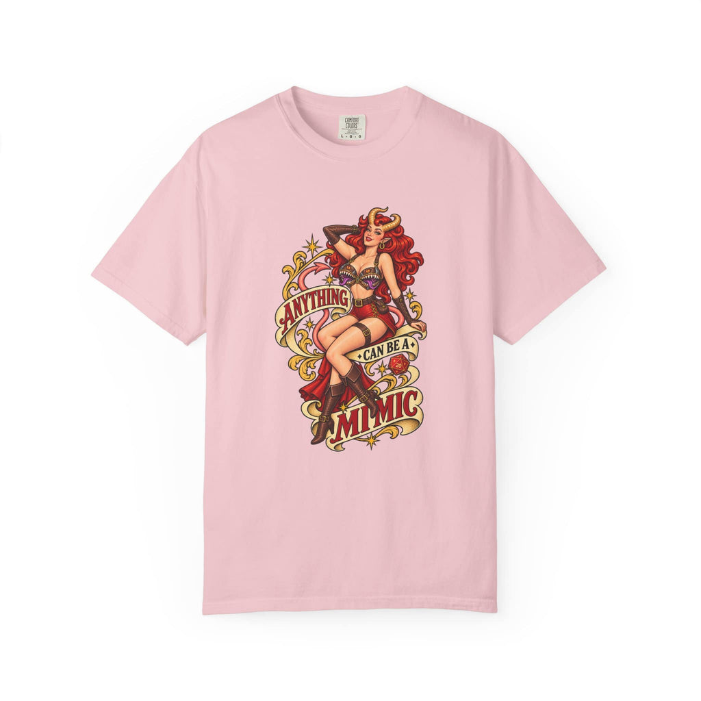 A light pink short-sleeve crewneck t-shirt featuring a vintage-style pin-up graphic on the front. The graphic depicts a woman with red hair in a red and black outfit, surrounded by decorative elements and the text 'ANYTHING CAN BE A MIMIC.
