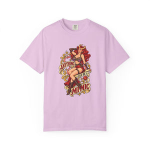 A light purple short-sleeve crewneck t-shirt featuring a vintage-style pin-up graphic on the front. The graphic depicts a woman with red hair in a black and red outfit, with retro text reading 'ANYTHING CAN BE A MIMIC' in red, yellow, and black.