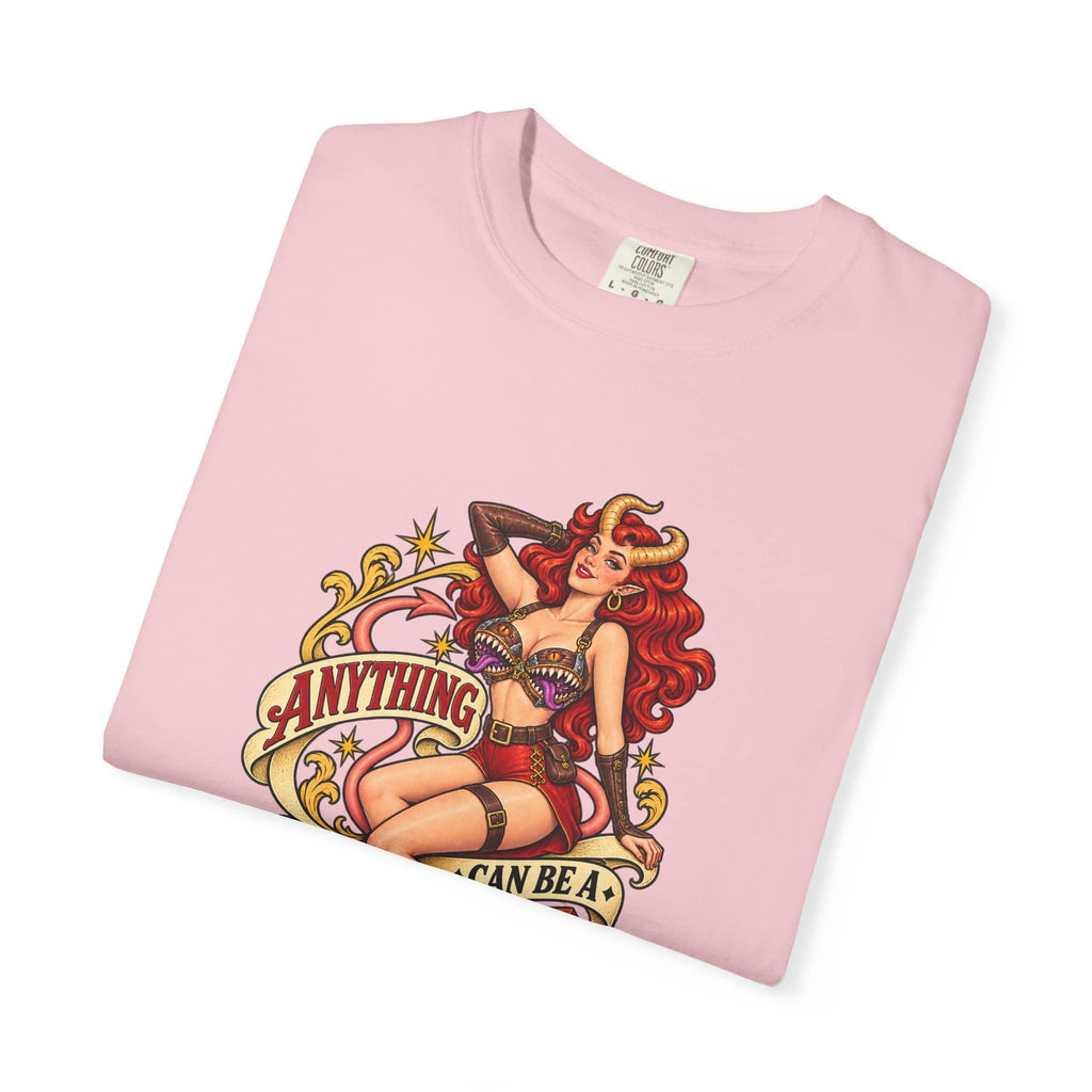 A folded light pink t-shirt with a vintage-style pin-up graphic of a red-haired woman with horns and the text 'ANYTHING CAN BE A MIMIC'.