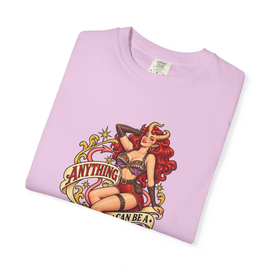 A light purple folded t-shirt with a colorful graphic print of a pin-up style woman with red hair and horns, with banners reading 'ANYTHING' and 'CAN BE A MIMIC'.