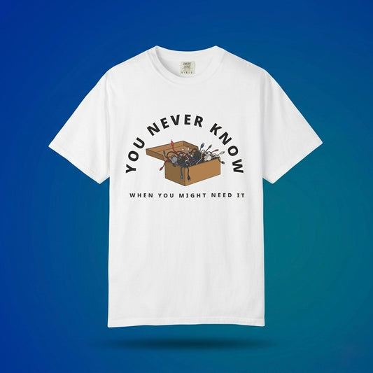 White graphic t-shirt flat lay on blue background featuring box of random cables.