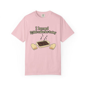 A light pink garment-dyed t-shirt featuring a cartoon of smoking brownies and the joke "I burned 2,000 calories today."