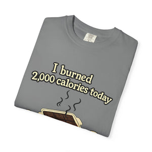 A folded grey t-shirt with a sarcastic baking meme graphic showing a tray of overcooked brownies and oven mitts.