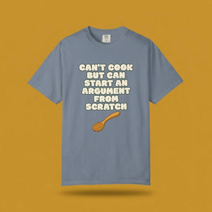 Blue graphic t-shirt flat lay on yellow background featuring Can’t Cook slogan.
