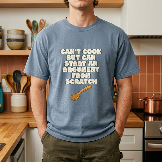 Blue graphic t-shirt flat lay on yellow background featuring Can’t Cook slogan.