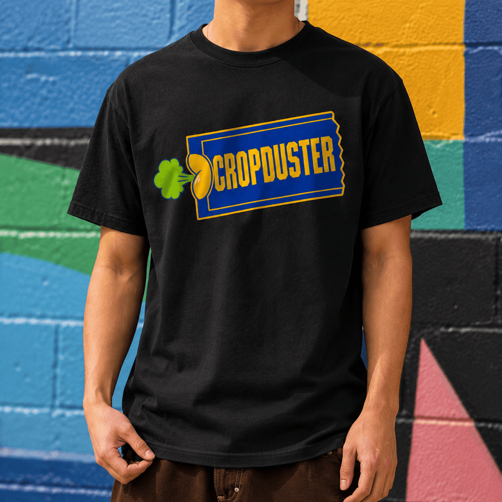 A close-up lifestyle shot of a model wearing a black graphic tee with a 90s video store ticket parody design, standing against a colorful blue and yellow painted brick wall.