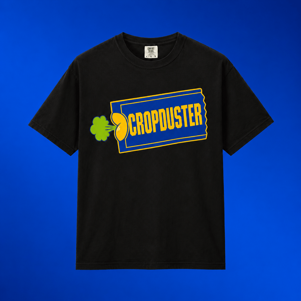 Flat lay mockup of the black Cropduster pop culture joke shirt centered on a vibrant royal blue gradient background.