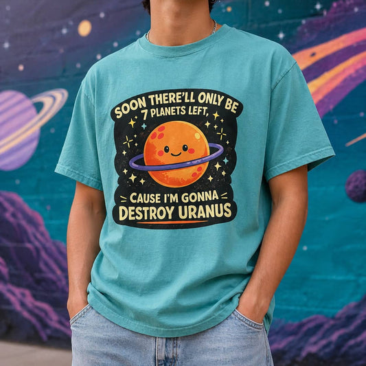 Male model standing outdoors in front of a space-themed mural wearing a teal Comfort Colors t-shirt with a cute planet graphic that says Soon there'll only be 7 planets left cause I'm gonna destroy Uranus.