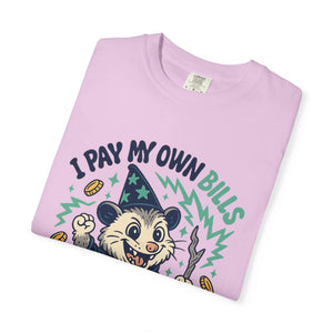 Folded pink t-shirt featuring a cartoon possum wizard holding a staff with funny text about paying bills