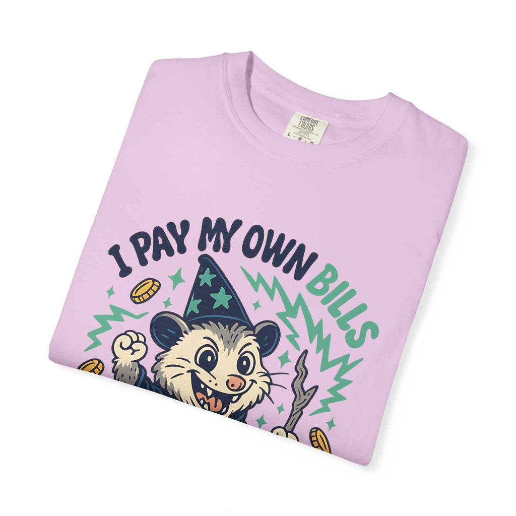 Folded pink t-shirt featuring a cartoon possum wizard holding a staff with funny text about paying bills
