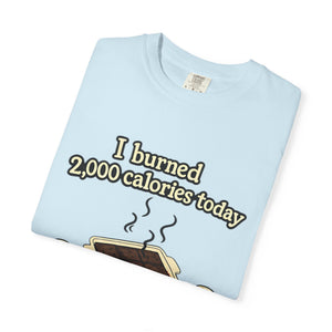 A neatly folded light blue Comfort Colors t-shirt featuring a cartoon of a smoking brownie pan and the text "I burned 2,000 calories today."