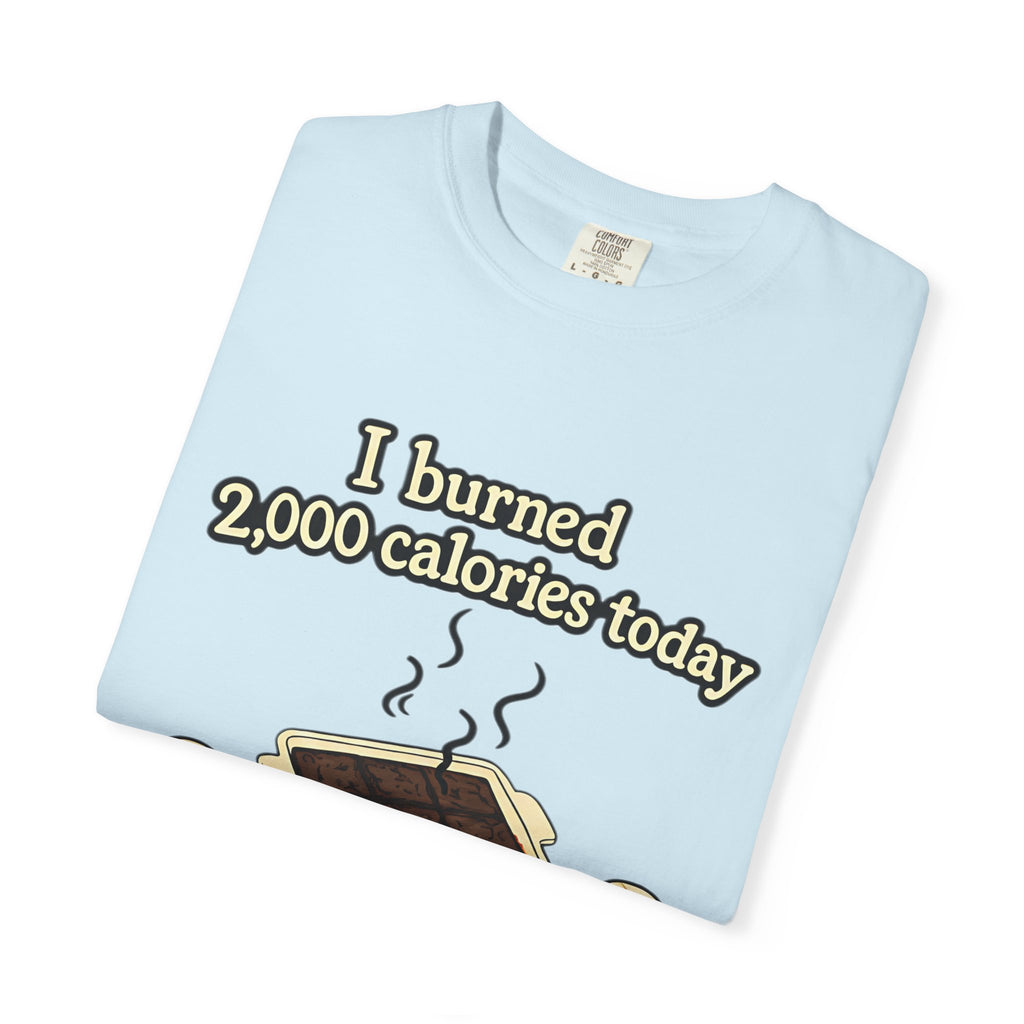 A neatly folded light blue Comfort Colors t-shirt featuring a cartoon of a smoking brownie pan and the text "I burned 2,000 calories today."