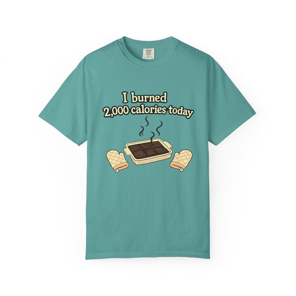 Flat lay view of a teal-colored t-shirt with a sarcastic baking graphic showing overdone brownies and the phrase "I burned 2,000 calories today."