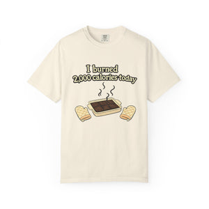 A cream-colored t-shirt featuring a high-quality graphic of a kitchen baking mishap and the caption "I burned 2,000 calories today."