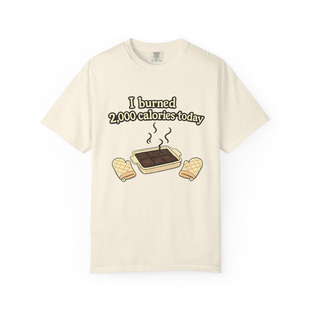 A cream-colored t-shirt featuring a high-quality graphic of a kitchen baking mishap and the caption "I burned 2,000 calories today."