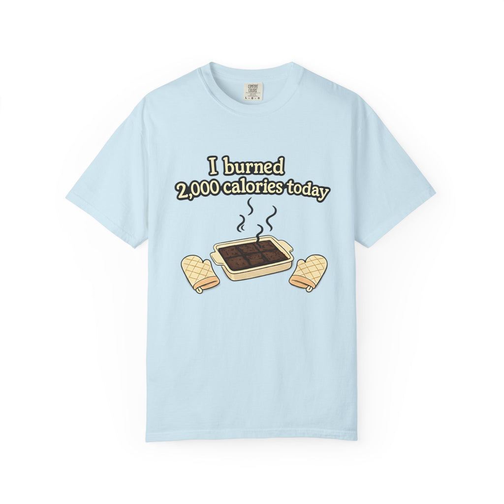 A flat lay of a light blue t-shirt featuring a funny "I burned 2,000 calories today" baking meme with a smoking brownie pan graphic.