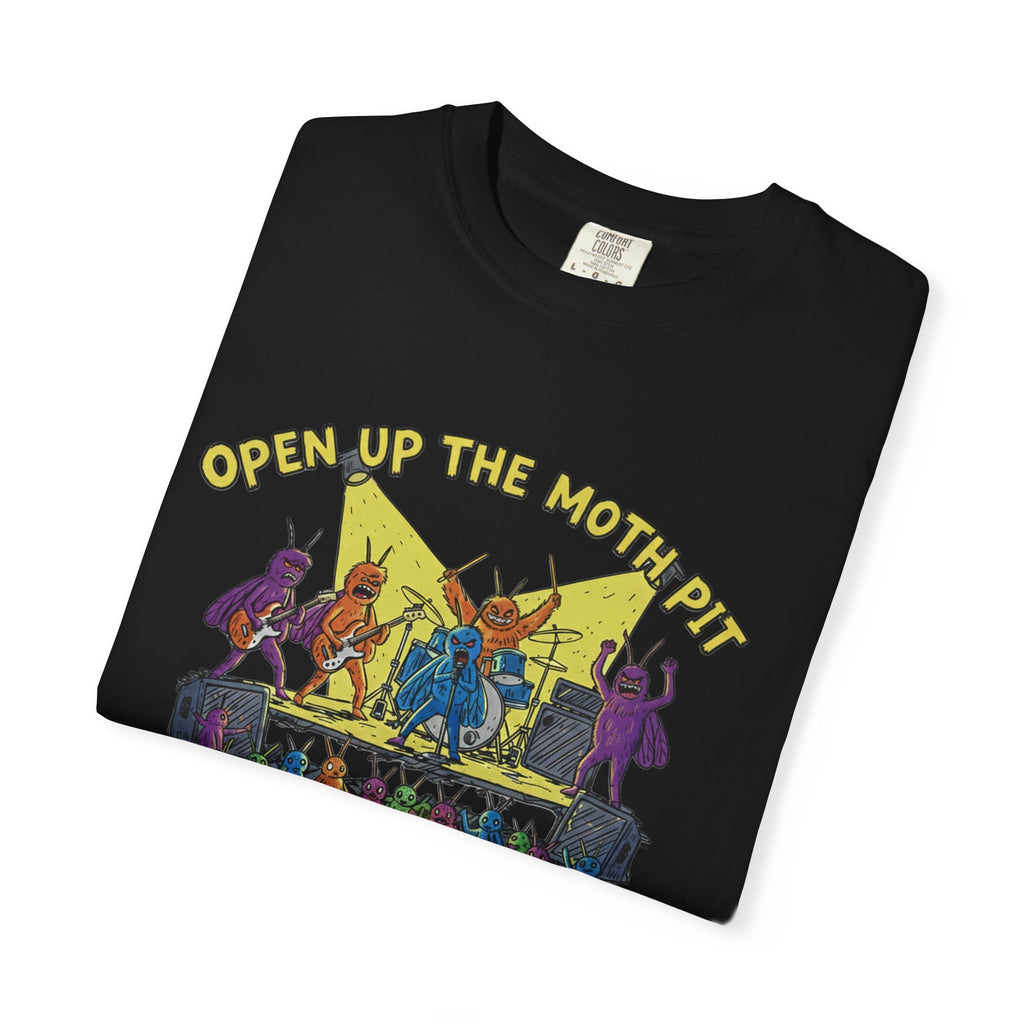 A black Comfort Colors t-shirt neatly folded, displaying the vibrant "Open Up The Moth Pit" illustration with electric guitar-playing moths and a moth drummer on a concert stage.