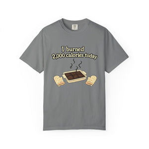 A flat lay of a grey short-sleeve t-shirt with a humorous illustration of a tray of burnt brownies and a calorie-counting joke.
