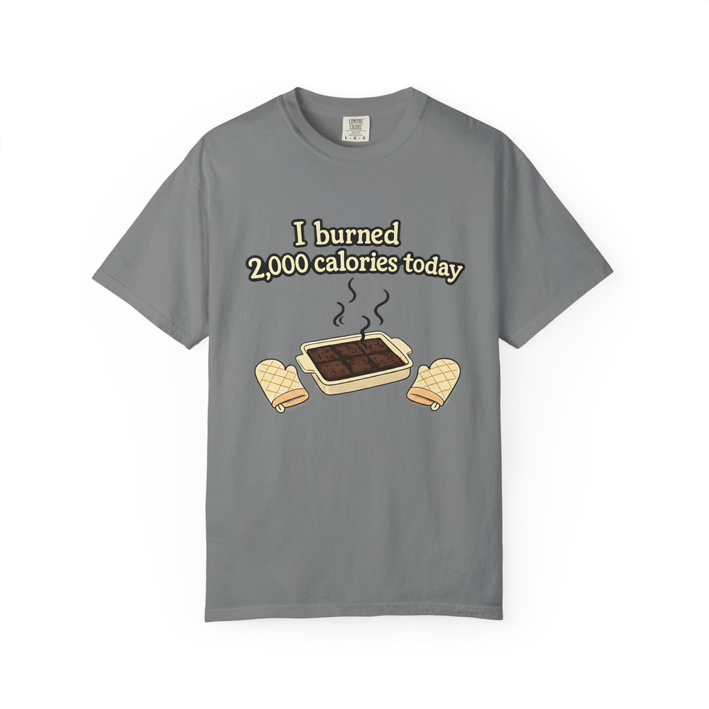 A flat lay of a grey short-sleeve t-shirt with a humorous illustration of a tray of burnt brownies and a calorie-counting joke.