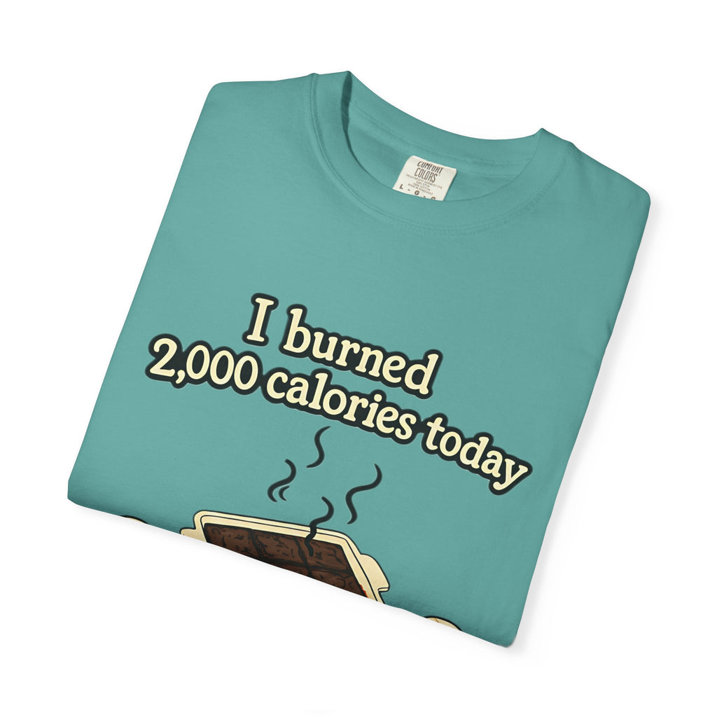 A folded teal or lagoon blue t-shirt displaying a graphic of burnt brownies in a pan with the humorous quote "I burned 2,000 calories today."