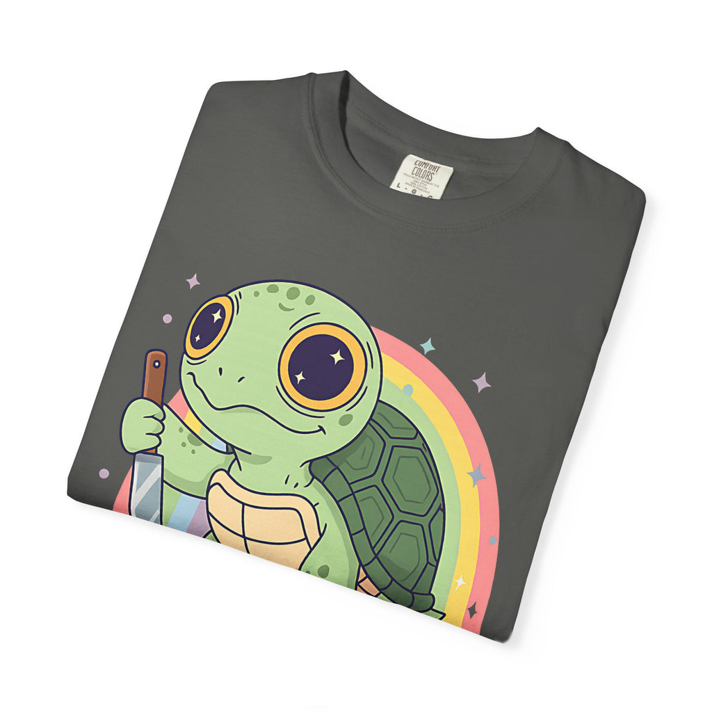 Flat lay of a folded pepper Comfort Colors t-shirt featuring a cartoon turtle holding a knife with a rainbow background.