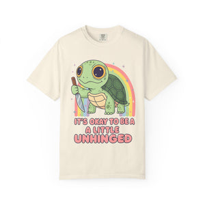 Ivory t-shirt featuring a cute green turtle holding a knife with the text "It's Okay To Be A Little Unhinged".